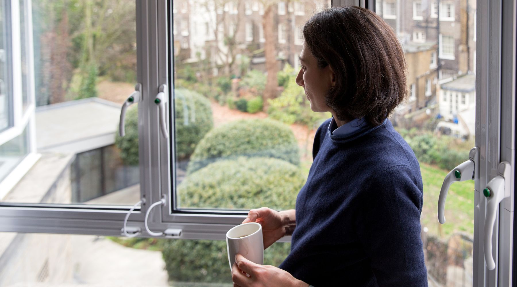 Guest with a mug looks out from a hotel window onto a leafy Bloomsbury garden courtyard at Imperial London Hotels.