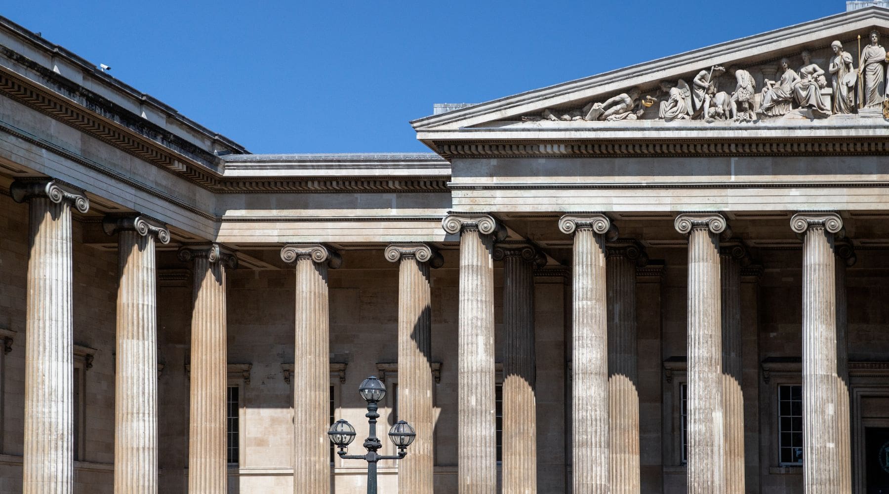 Front facade of the British Museum with grand stone columns and detailed frieze beneath a clear blue sky