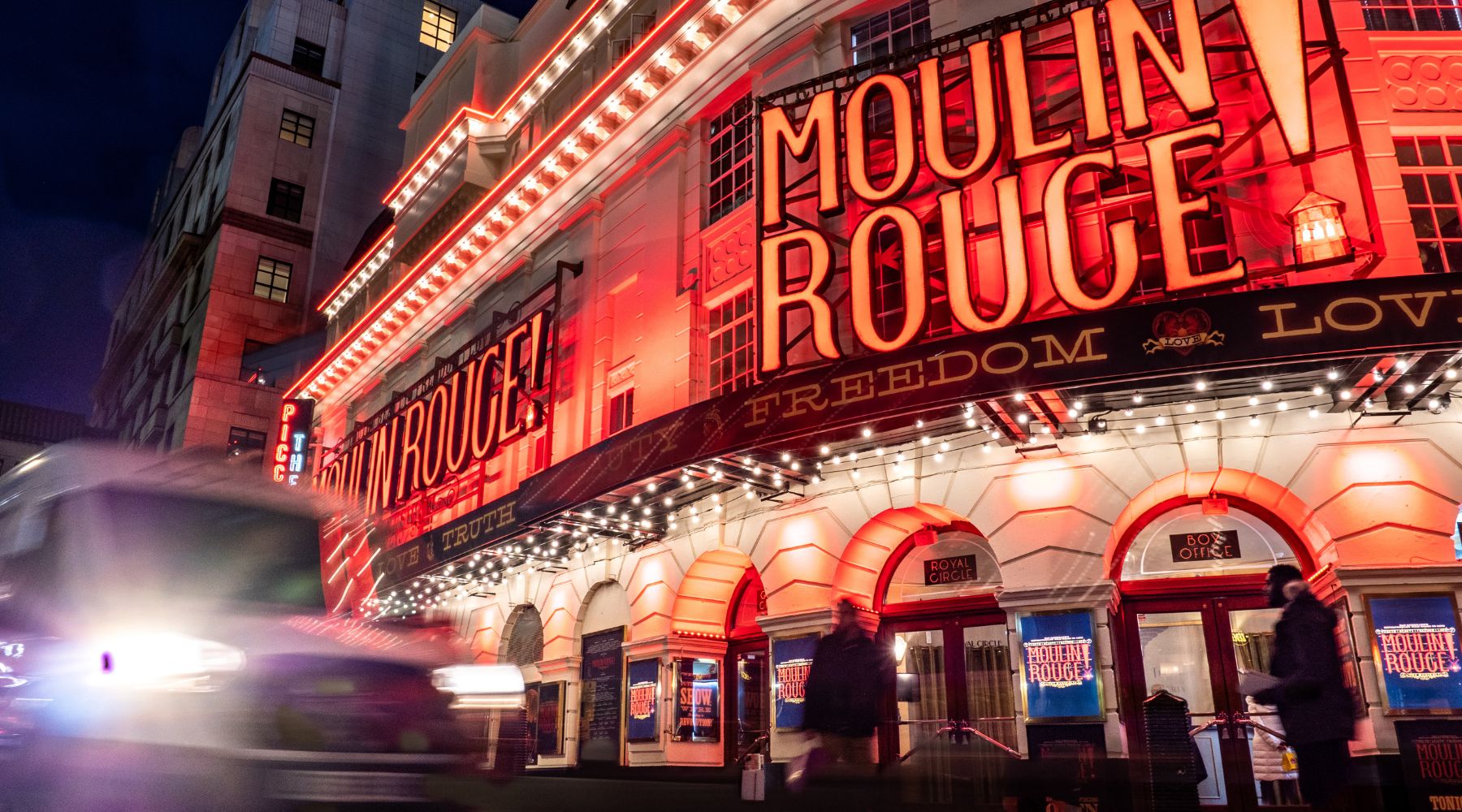 Bright red “Moulin Rouge! The Musical” marquee at London’s Piccadilly Theatre at night, with blurred traffic and people outside