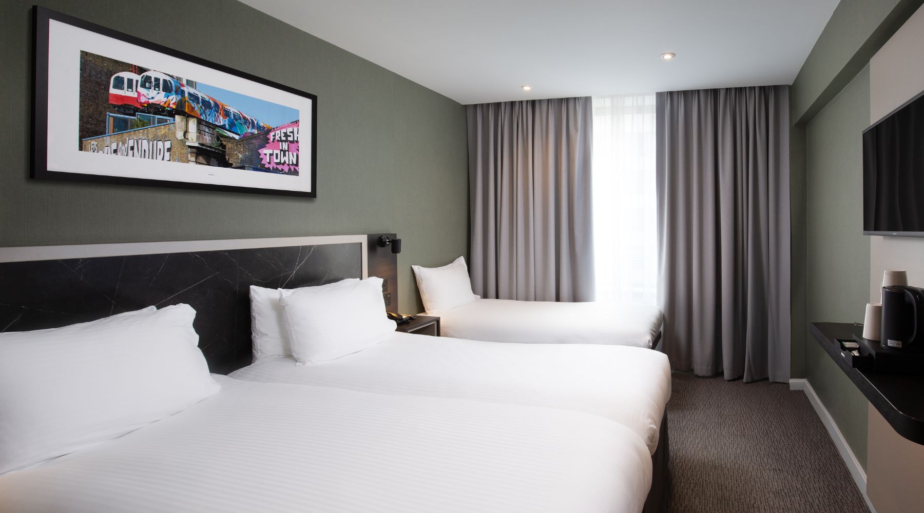 Family room with three beds, grey curtains, wall art and TV in the Royal National Hotel.