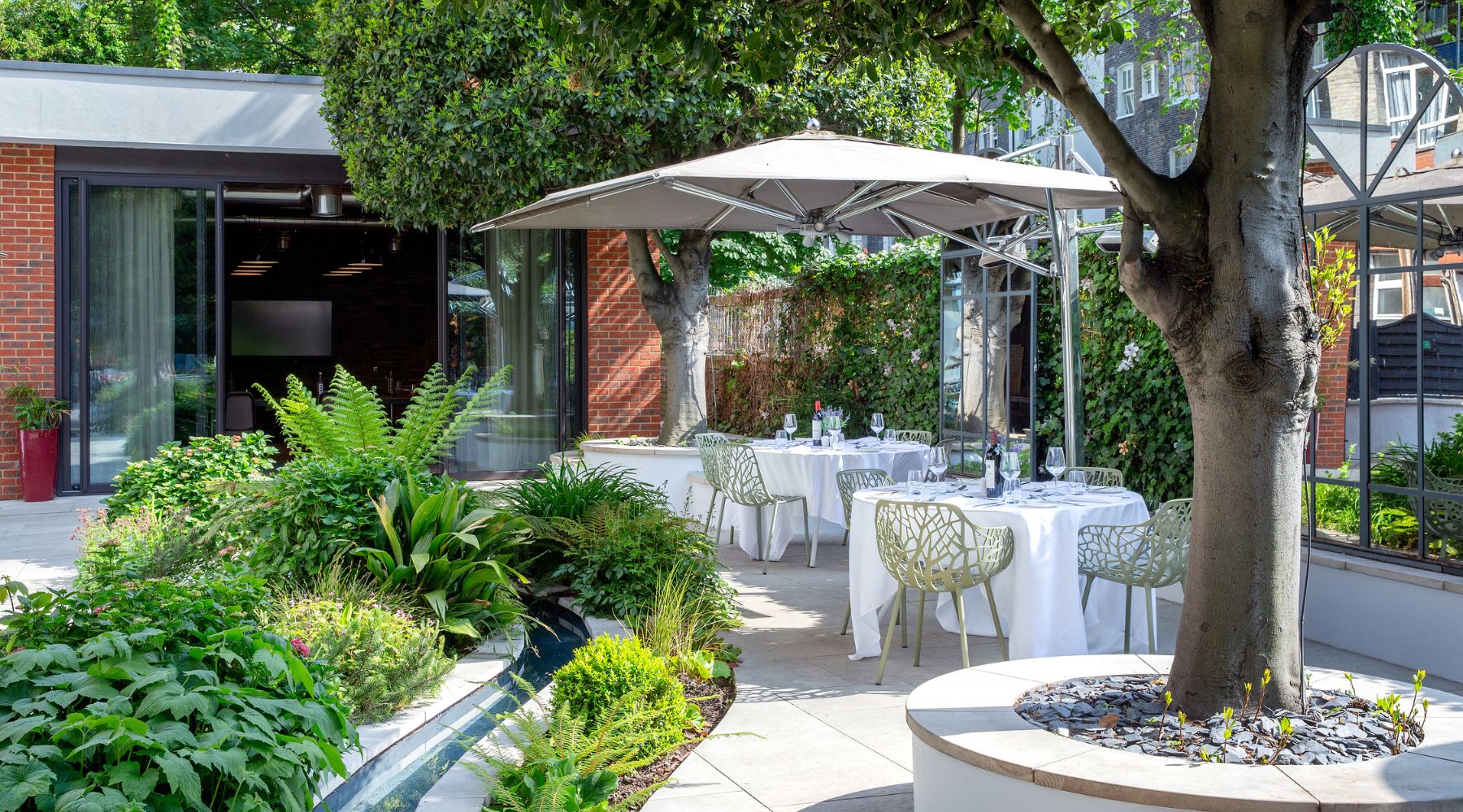  Peaceful garden terrace with outdoor dining tables, greenery and parasols at Imperial London Hotels in Bloomsbury.
