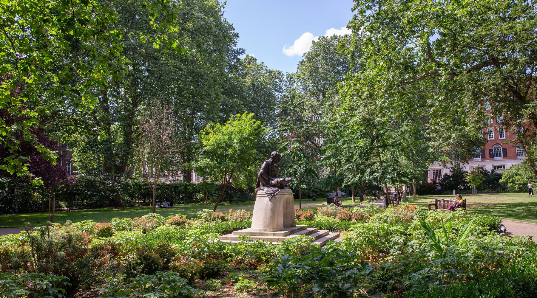 Statue set within a lush Bloomsbury garden square, surrounded by greenery, flower beds and mature trees.