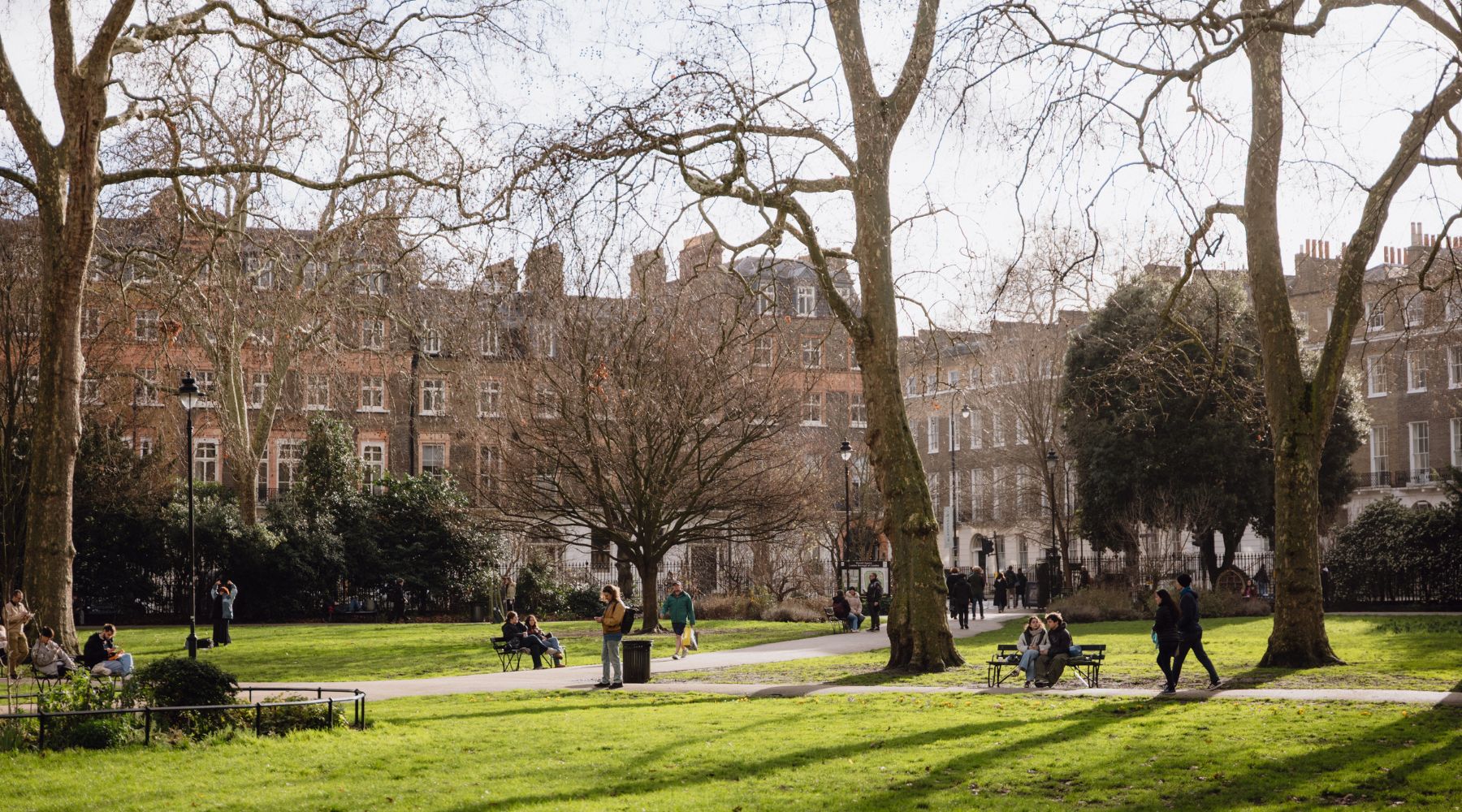 Leafy Bloomsbury garden square with people strolling and relaxing on benches, surrounded by Georgian townhouses in central London.