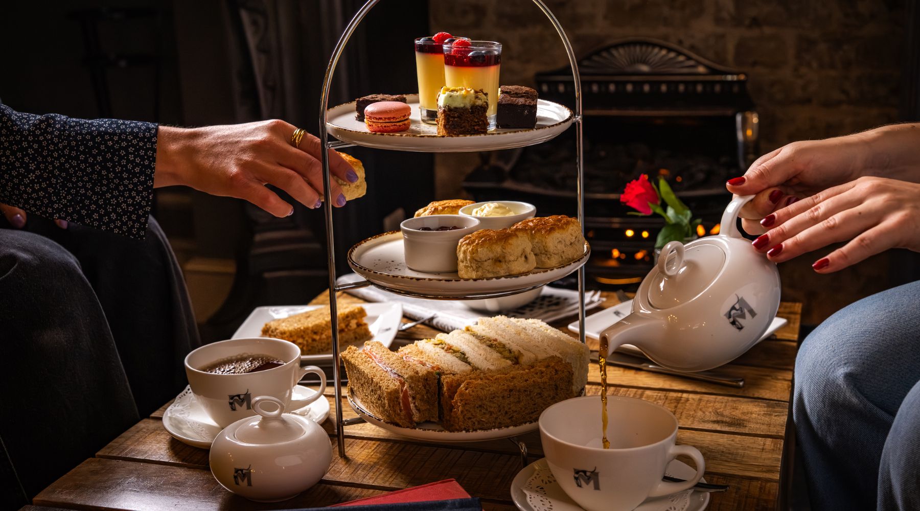 Afternoon tea set up with one person pouring the tea and another one picking up a scone.