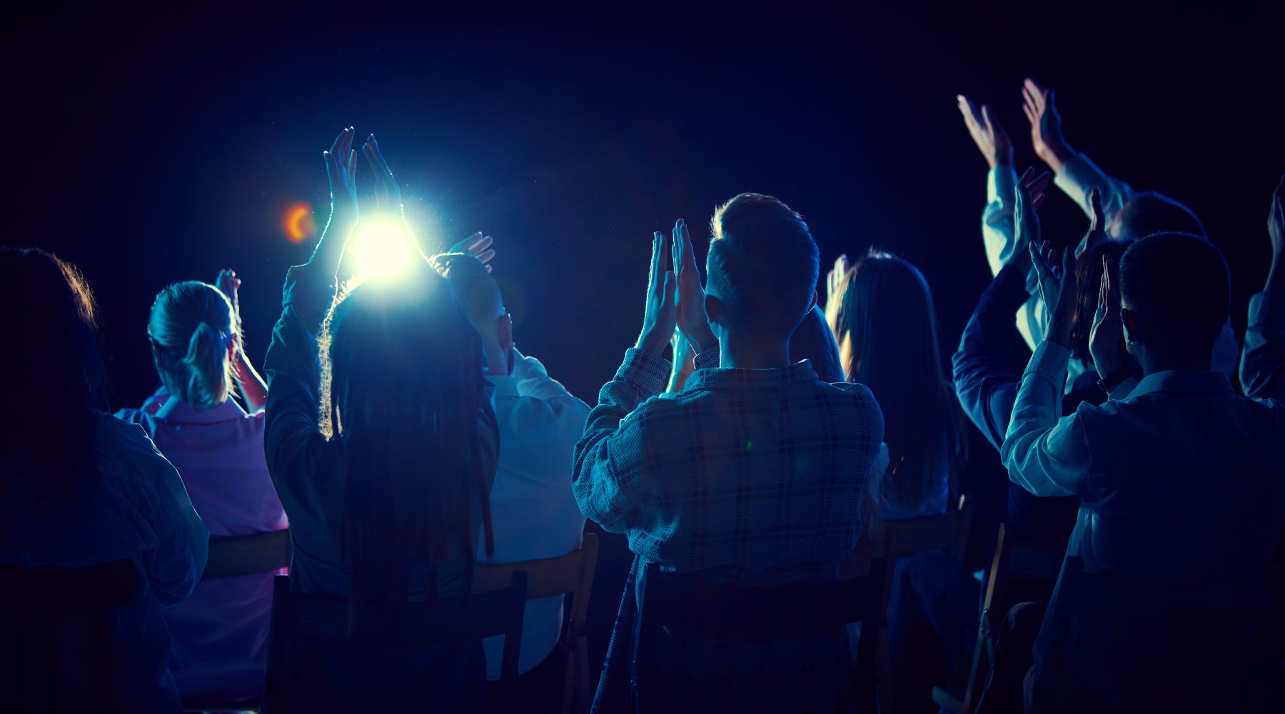 Audience applauding at a live performance, silhouettes clapping under bright stage lights in an intimate London venue.
